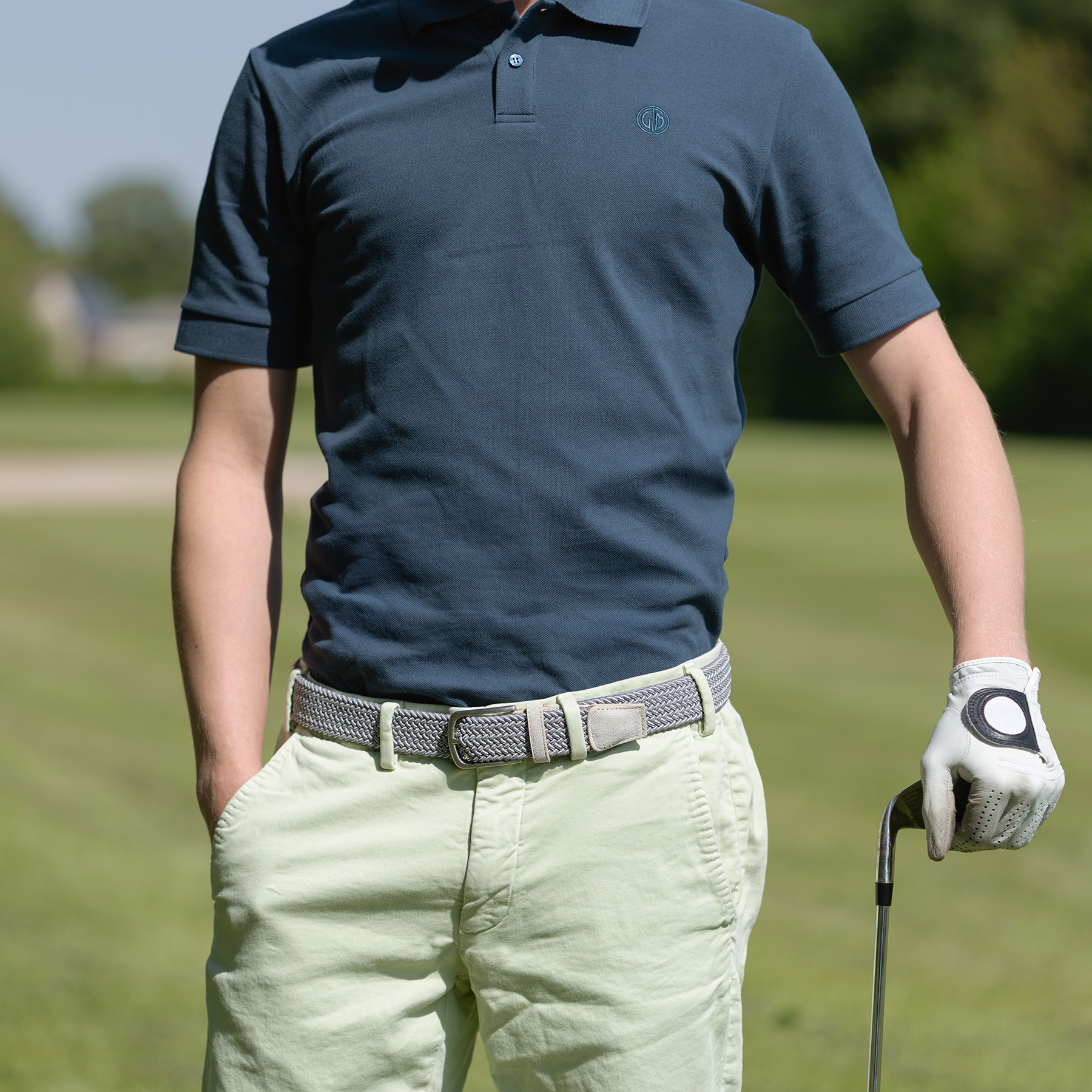 Bekleidung, Handschuh, Feld, Golfspieler im sportlich-eleganten Outfit mit grauem Lindenmann Stretchgürtel und dunkelblauem Lindenmann Poloshirt auf dem Golfplatz.