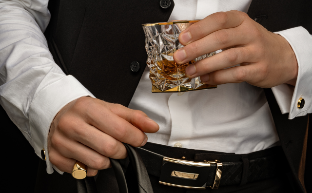 Mann in formeller Kleidung hält ein Glas Whisky und einen Gürtel