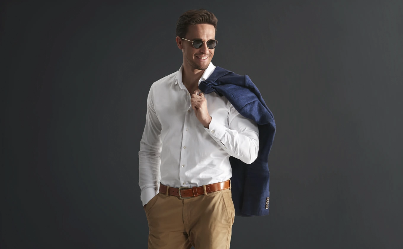 Mann in weissem Hemd und beiger Hose mit braunem Lederguertel und blauer Jacke ueber der Schulter Mann in weissem Hemd und beiger Hose mit braunem Lederguertel und blauer Jacke ueber der Schulter