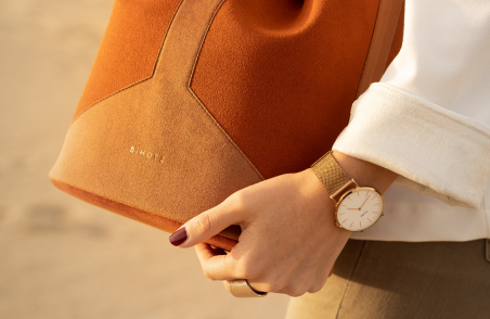 Frau trägt eine orangefarbene Tasche über der Schulter und eine goldene Uhr