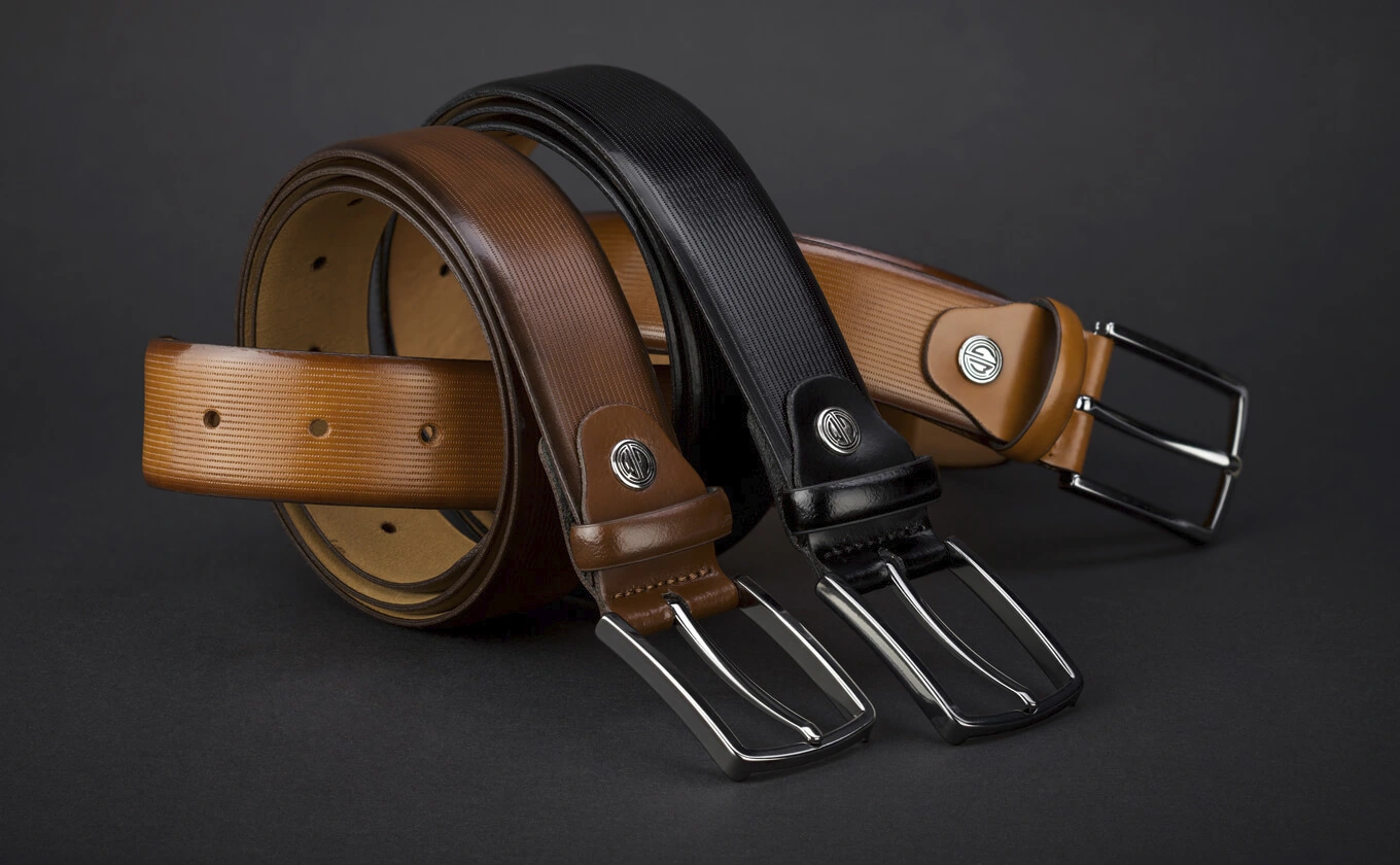 Drei Herren-Ledergürtel in Braun und Schwarz auf schwarzem Hintergrund Drei Herren-Ledergürtel in Braun und Schwarz auf schwarzem Hintergrund