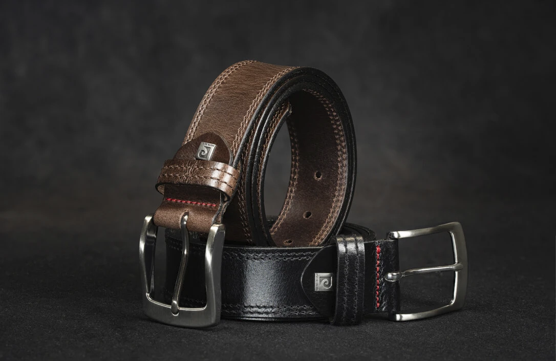 Zwei Pierre Cardin Herrengürtel aus Leder, einer in braunem Leder und der andere in schwarzem Leder, auf schwarzem Hintergrund arrangiert Zwei Pierre Cardin Herrengürtel aus Leder, einer in braunem Leder und der andere in schwarzem Leder, auf schwarzem Hintergrund arrangiert