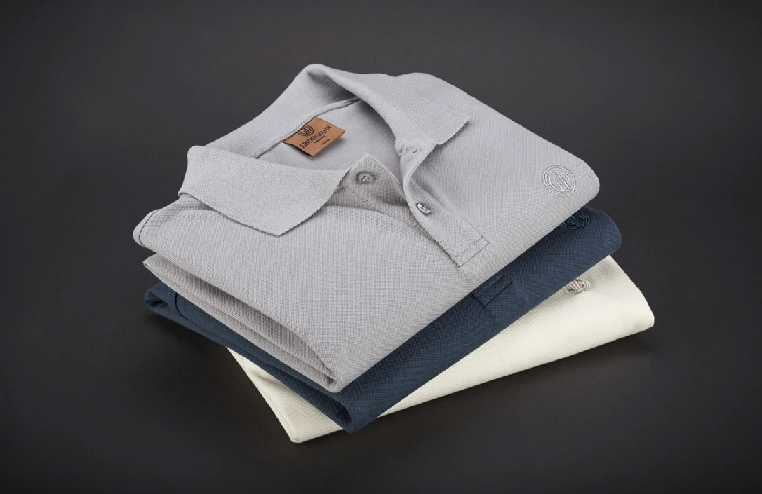 Drei gestapelte Polohemden, das oberste in Grau, darunter ein dunkelblaues und ein weißes Polohemd Drei gestapelte Polohemden, das oberste in Grau, darunter ein dunkelblaues und ein weißes Polohemd