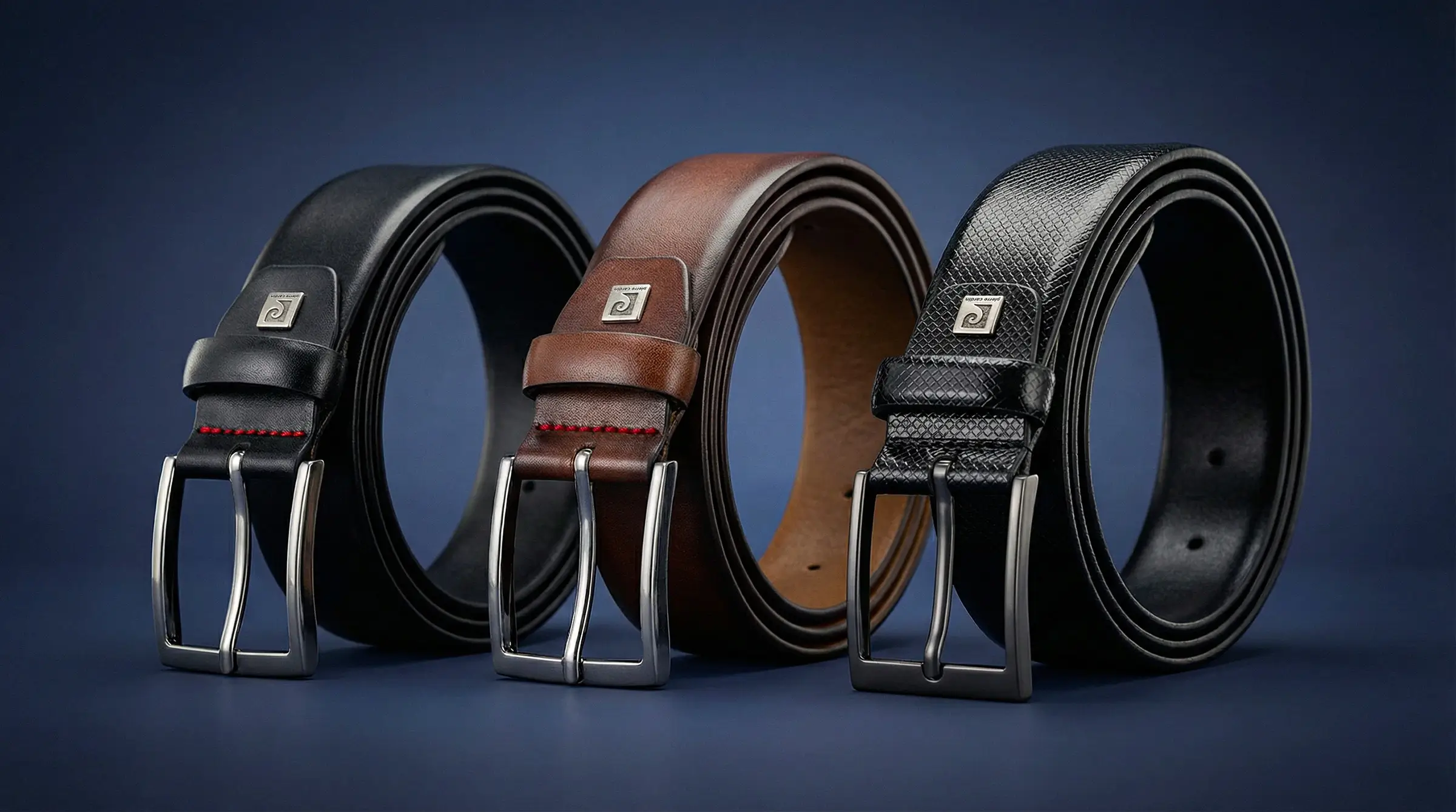 Drei pierre cardin Ledergürtel in Schwarz und Braun mit klassischen Metallschließen vor dunkelblauem Hintergrund